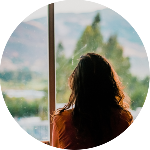 A woman looking out a window, appearing contemplative. This image represents the emotional challenges of anxiety that can be addressed through counselling in Vancouver.